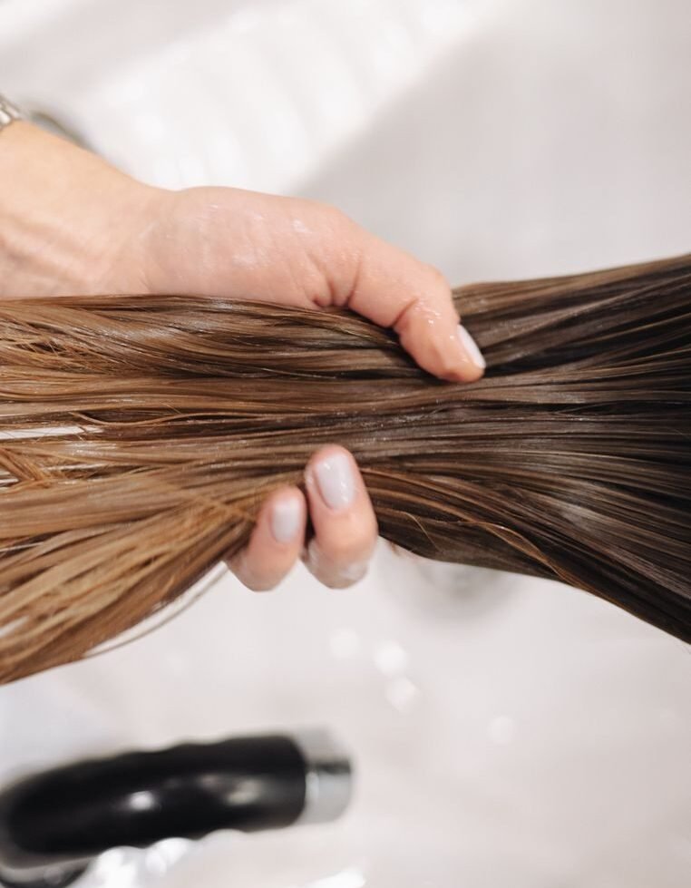 Hands running treatment through long wet hair over a basin