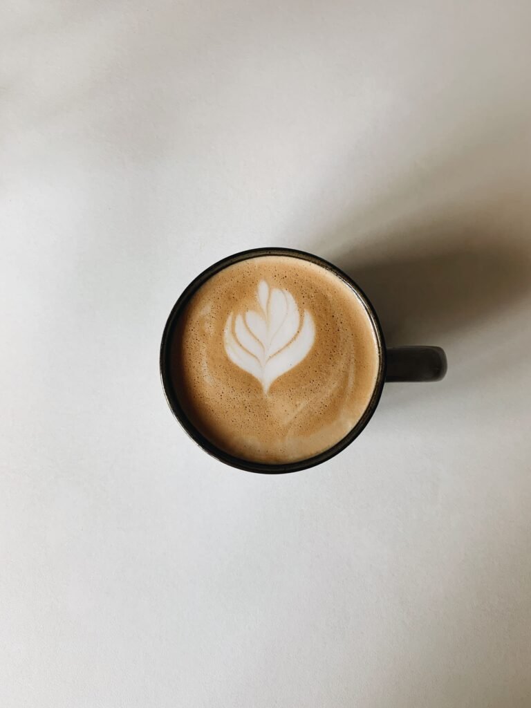 Latte art in a white cup seen from above, foam swirled into a leaf pattern