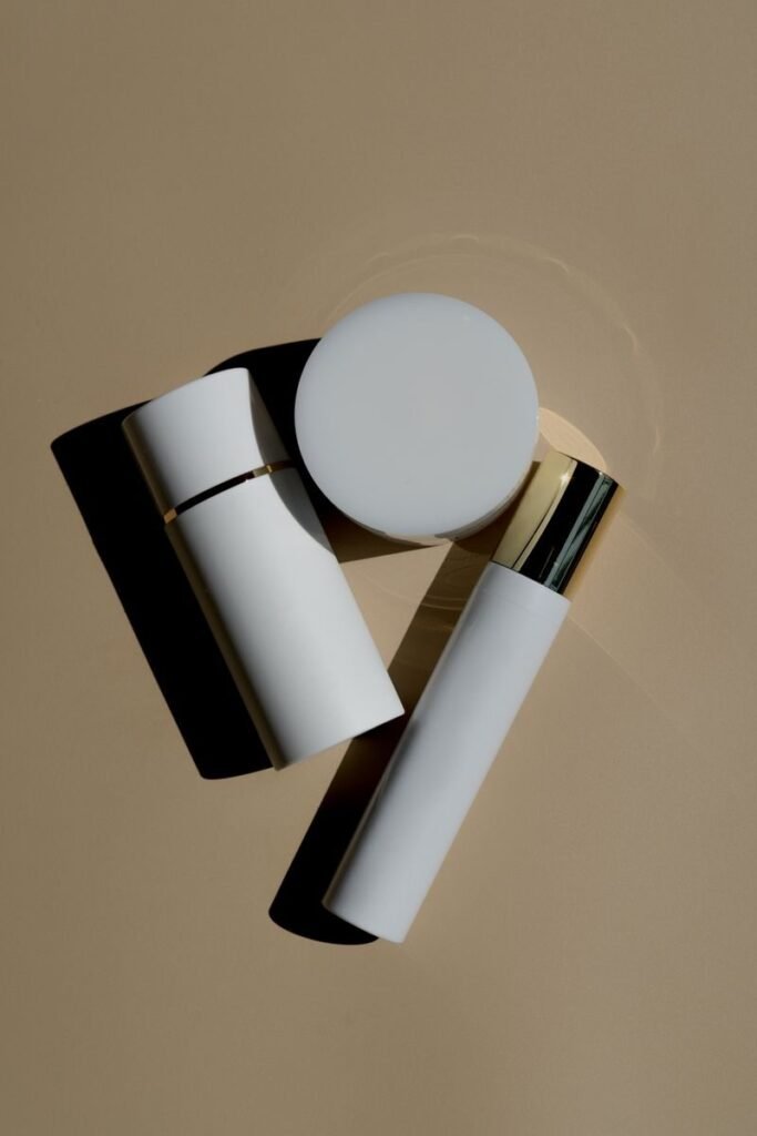 White and gold skincare bottles and a jar arranged on a warm tan surface