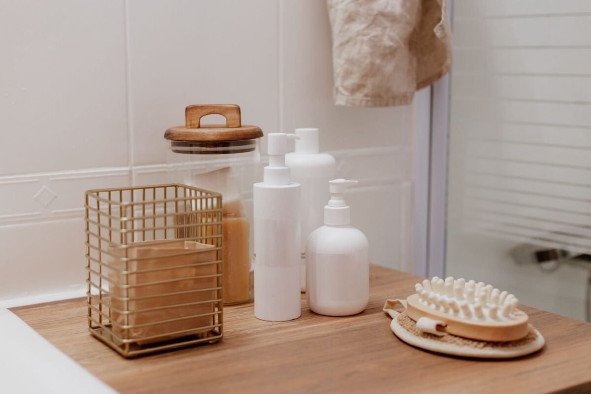 White skincare bottles and a wooden body brush on a bathroom shelf in warm light